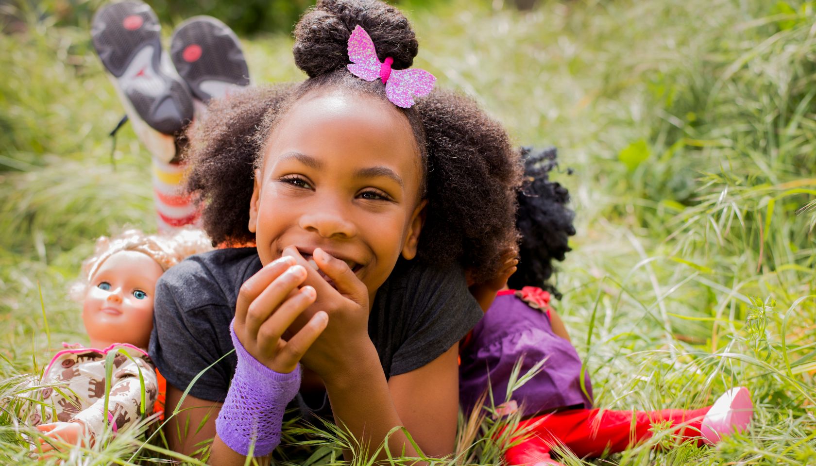 Black girl playing with dolls in tall grass