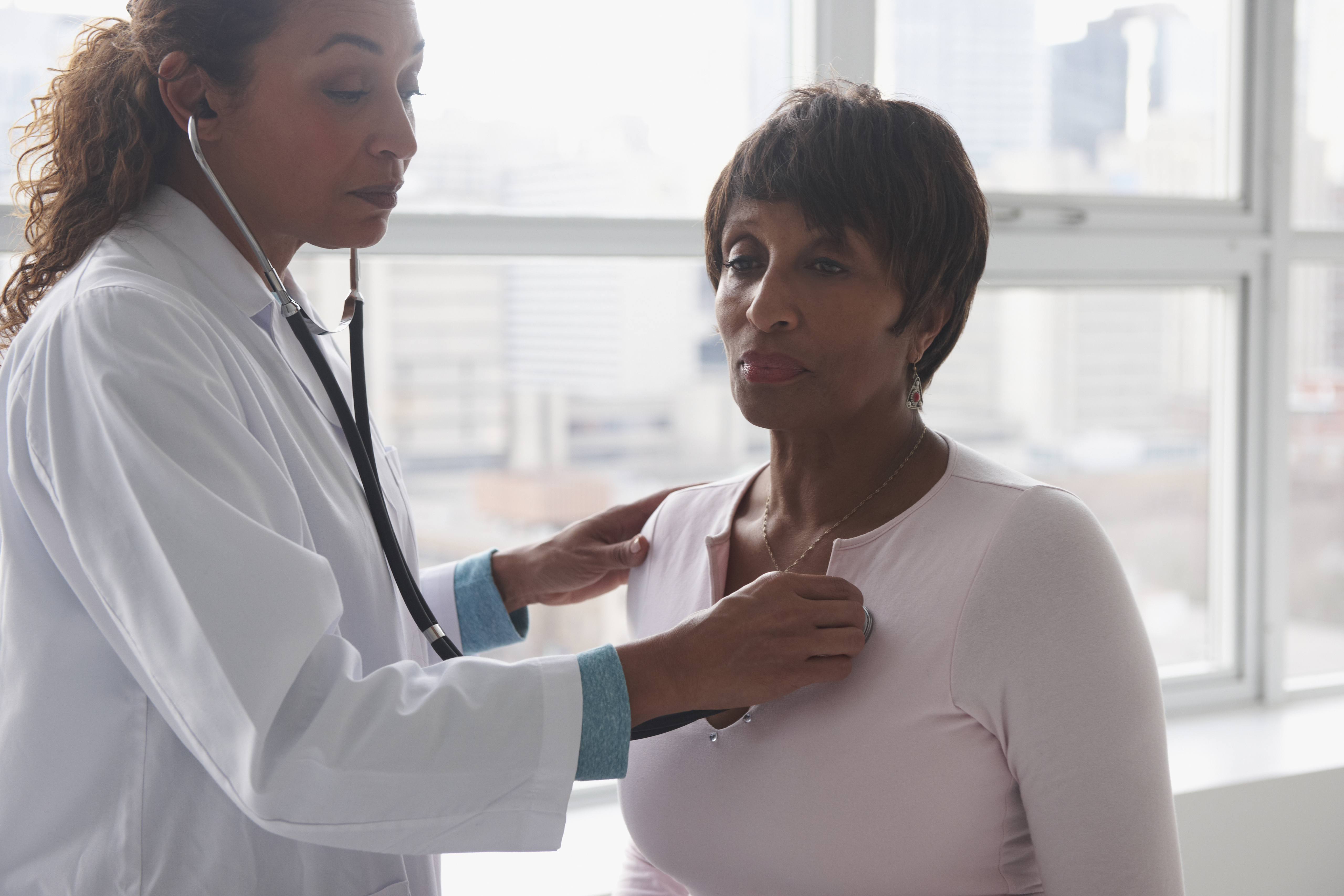 Doctor listening to heartbeat of patient near window