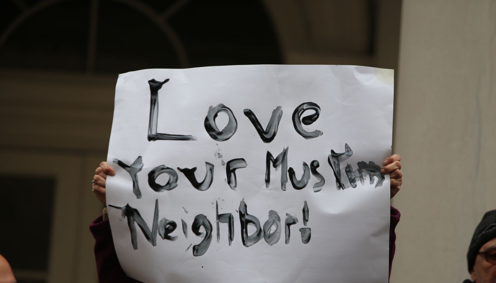 Hand-lettered Love Your Muslim Neighbor sign held aloft.