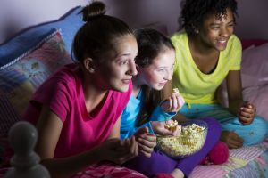 Preteen girls at sleepover watching tv, eating popcorn