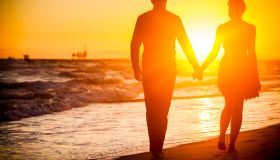 Diverse couple walking on beach at sunset