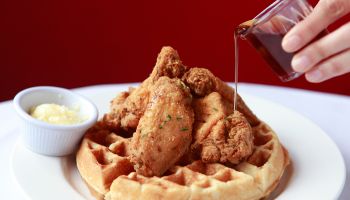 pouring syrup on fried chicken and waffles on restaurant table with butter